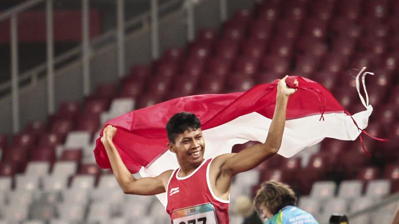 male Para athlete Sapto Yogo Purnomo running holding an Indonesia flag